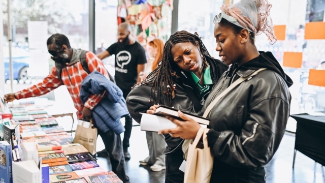 Two women look at a book they've picked up from a stand in front of them.