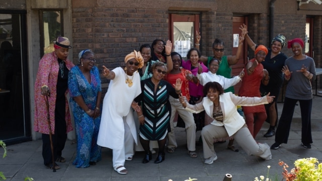 A group of over 50s Caribbean women, dressed in their finest, posing as a group.