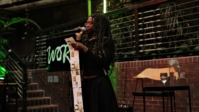 Poet Phoenix Yemi reads a poem from a long scroll of paper that reaches the floor.
