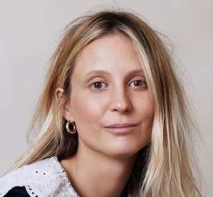 A light-skinned woman with long blond hair against a cream coloured background.